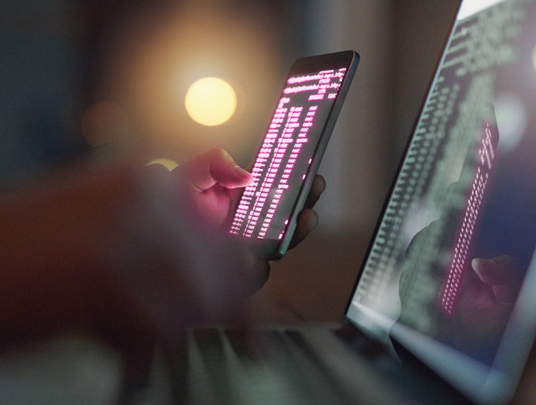 Person looking at computer code on phone and laptop.