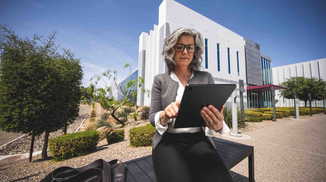 A civilian agency worker sits outside a building and reviews information on a 5G-connected tablet.