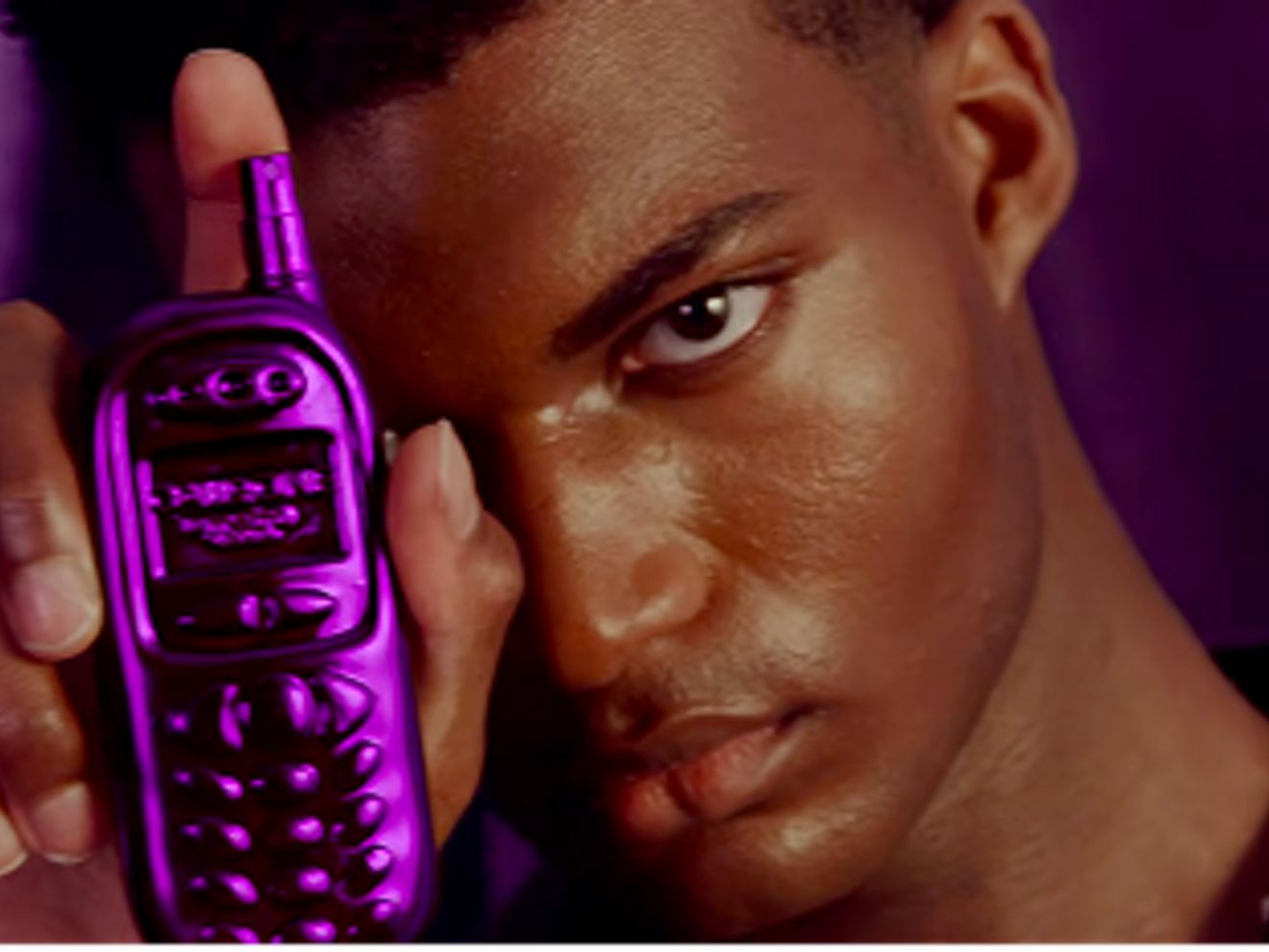 Un hombre sostiene un frasco de perfume morado con forma de celular de principios de 2000.