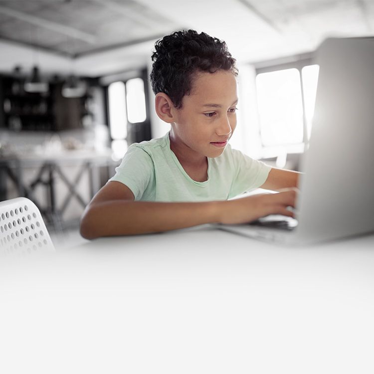 A child sits at a kitchen table and uses a laptop.