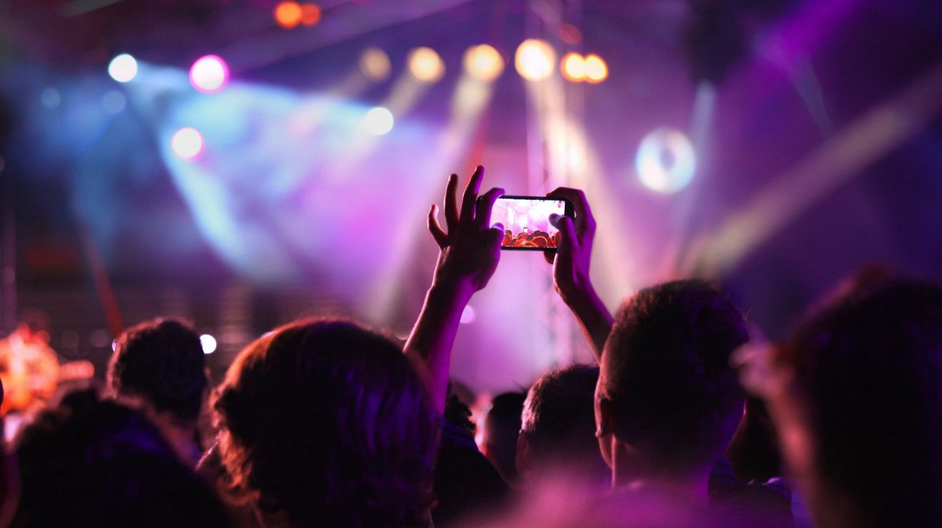 A person in a crowd holds up their smartphone to take a picture during a show.