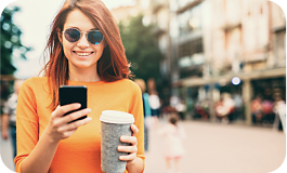 Smiling person looking at their phone while they drink coffee.