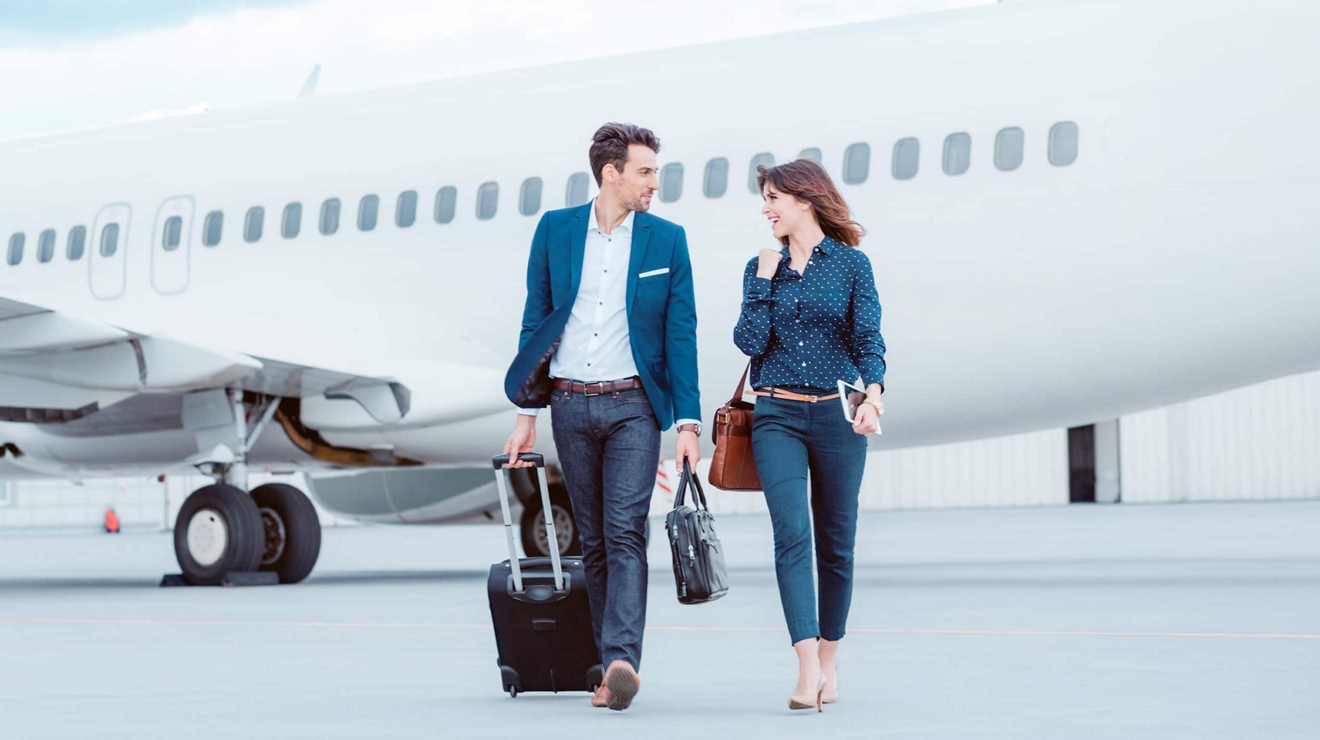 Two business travelers cross a tarmac in front of a commercial airliner.