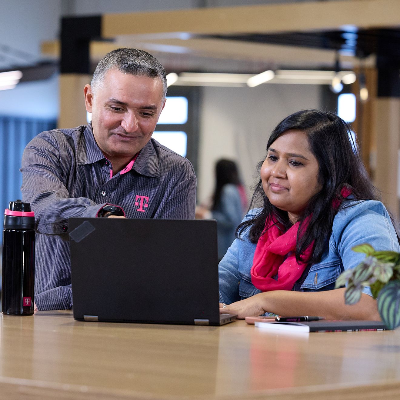 Two T-Mobile employees are sitting together smiling as they look at a laptop screen. 