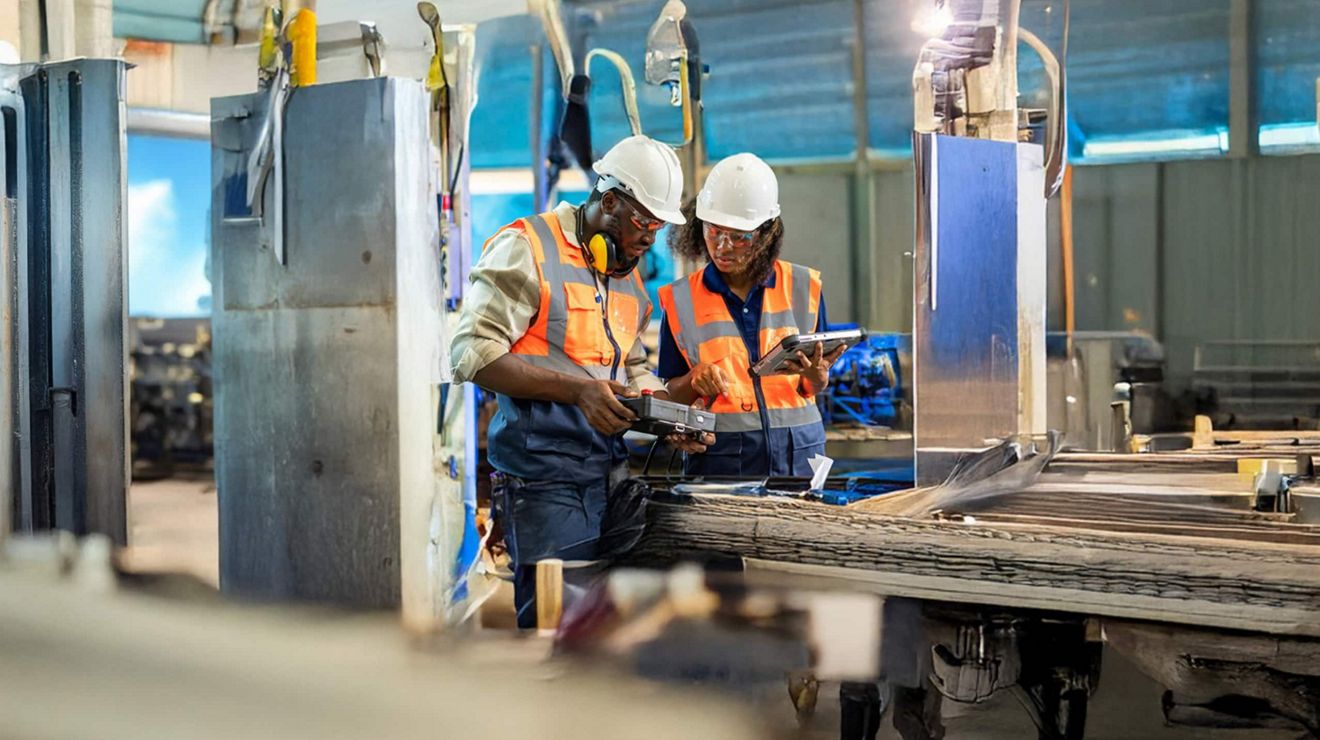 Two mechanical engineers in hardhats use T-Mobile-connected equipment to fix industrial machinery. 