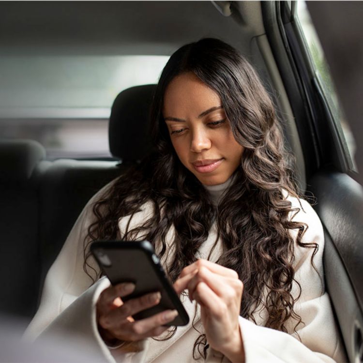 Young woman scrolls through content on phone while riding in back seat of car.