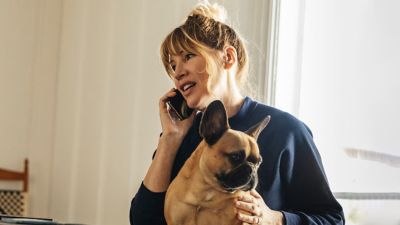 Woman chats on phone while patting her French bulldog.