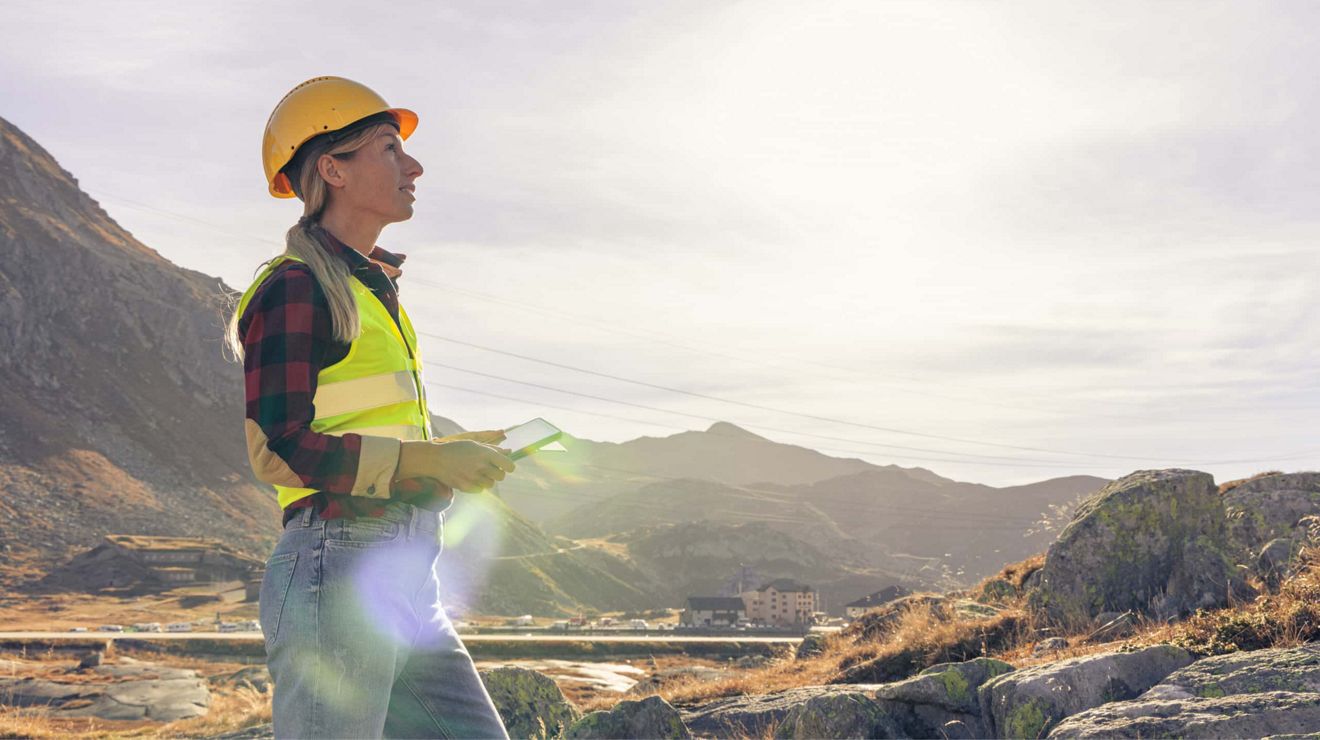 A utility worker with a digital tablet looks out at the horizon in a remote location.