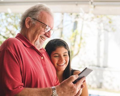 An older man and a young girl looking at a tablet, leaning in and laughing.