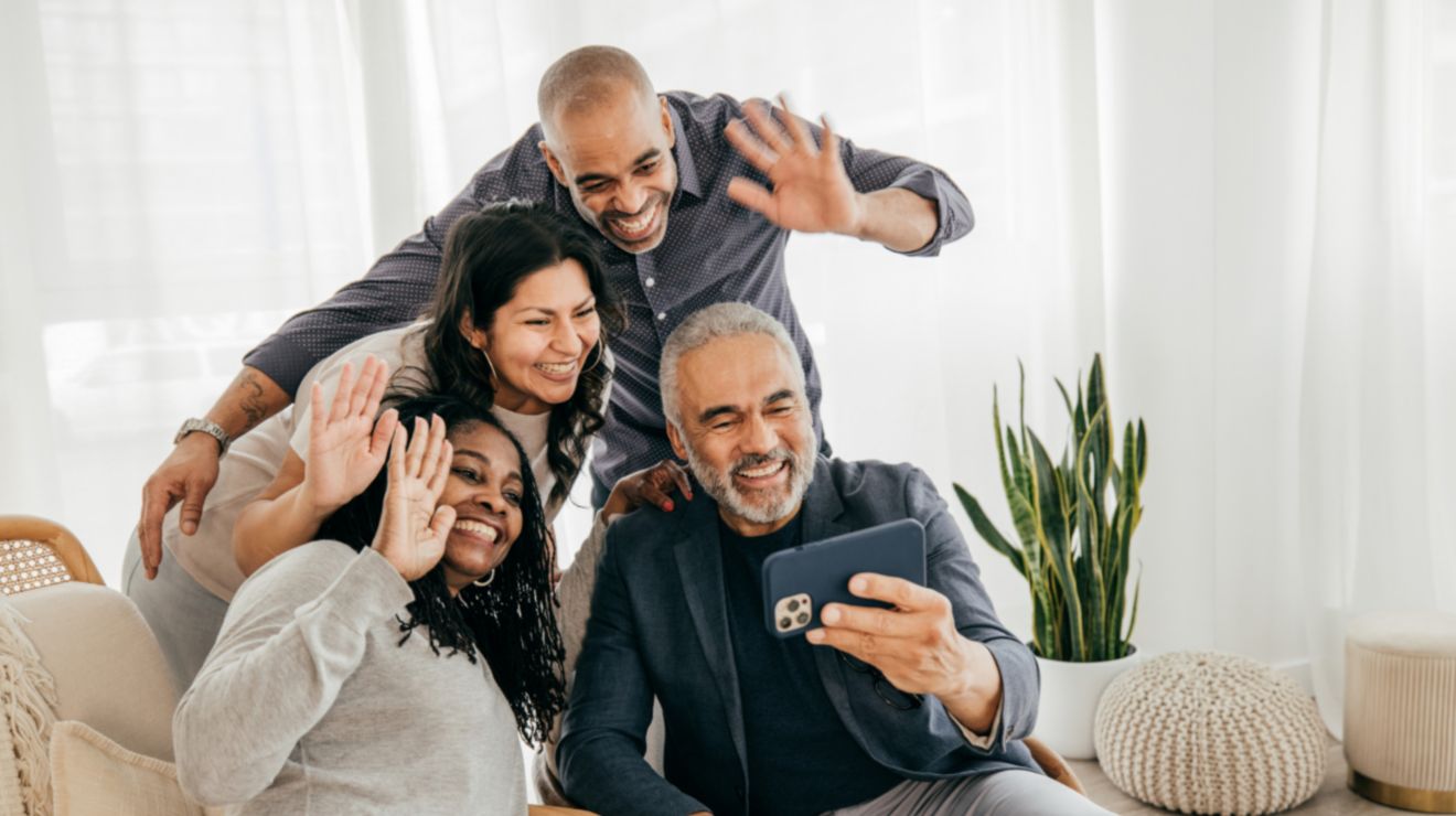 Family members crowd around a phone and wave hello.