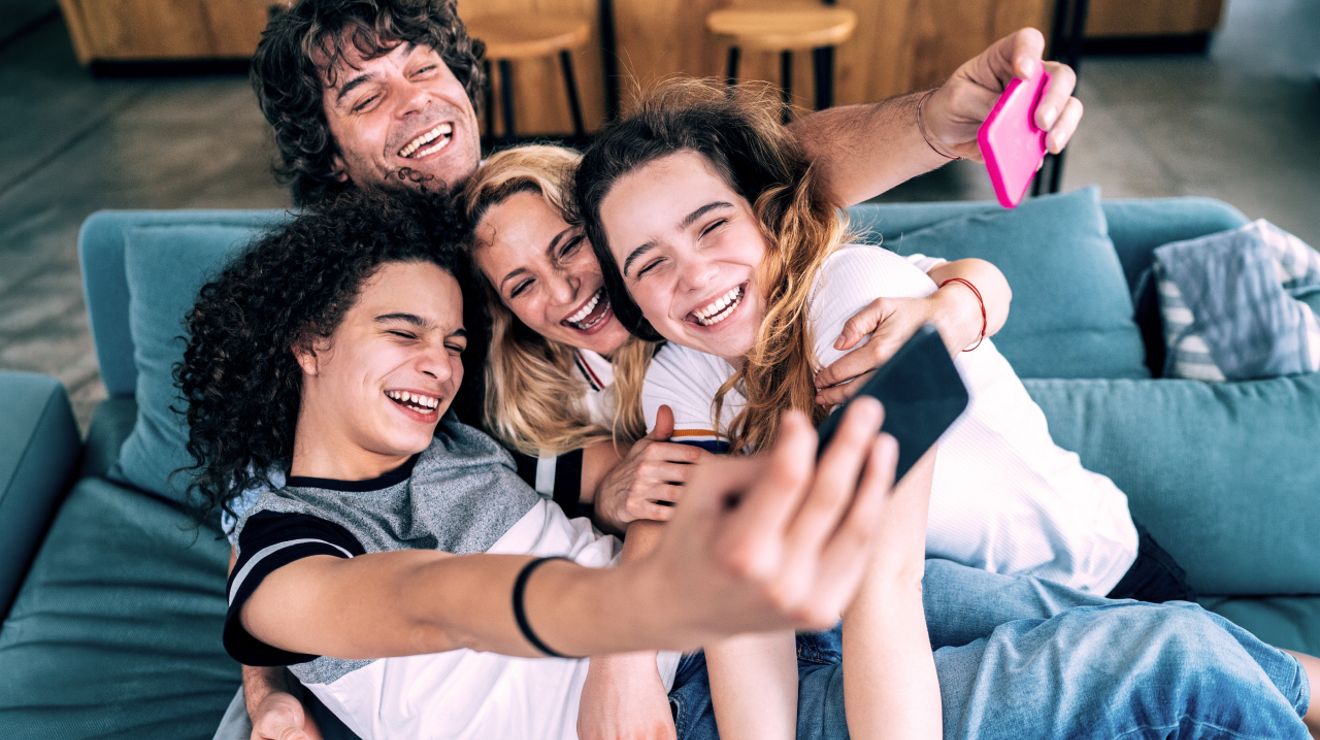 Group of four friends laughing and taking a selfie together on a couch.