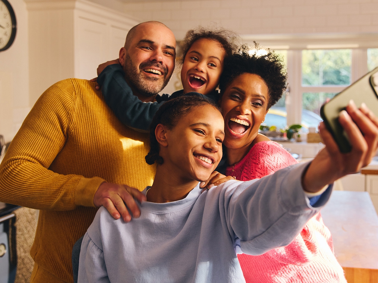 A smiling family of four clusters together for a selfie in their home.