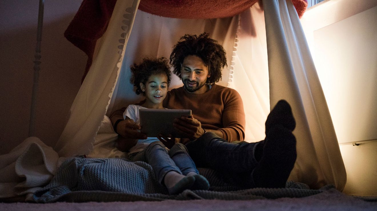 A man and a young girl smile as they look at a tablet.