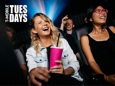 Two women sitting side by side at a movie theater, laughing.