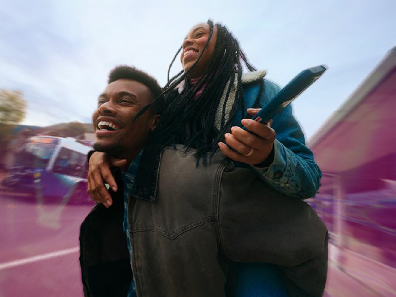 Dos amigos, uno de los cuales lleva al otro a caballito de forma divertida mientras sostienen un smartphone.