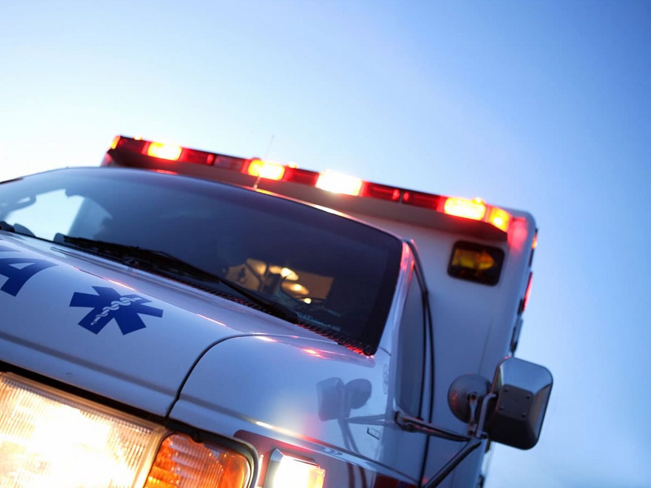 The front of an ambulance with its headlights and top flashing lights activated.