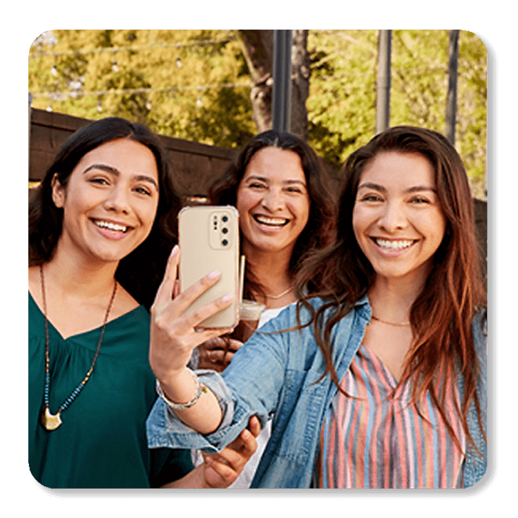 Three women smile for a selfie in a park