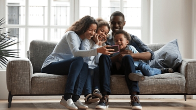 Family sitting on sofa gathered around a smartphone