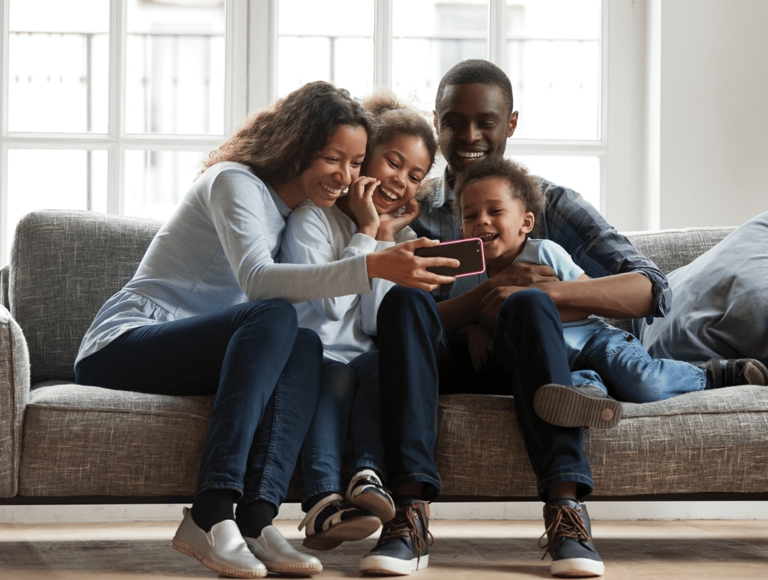 Family sitting on sofa gathered around a smartphone