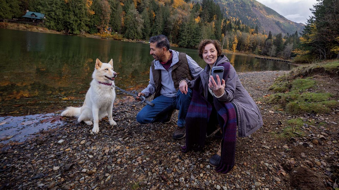 A couple takes a selfie with their dog next to a creek.