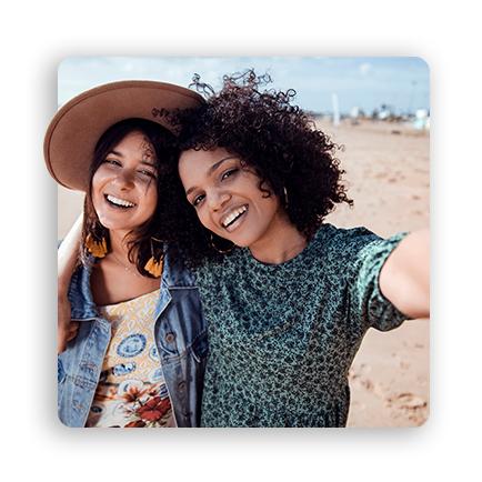 Two women on a beach, smiling as they take a selfie