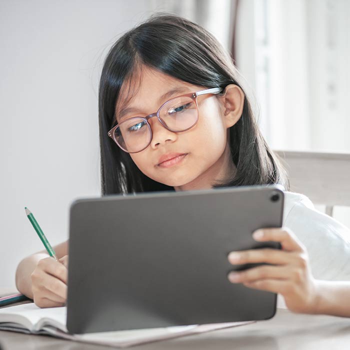 Student sitting in a chair while looking at a tablet and holding a pencil.