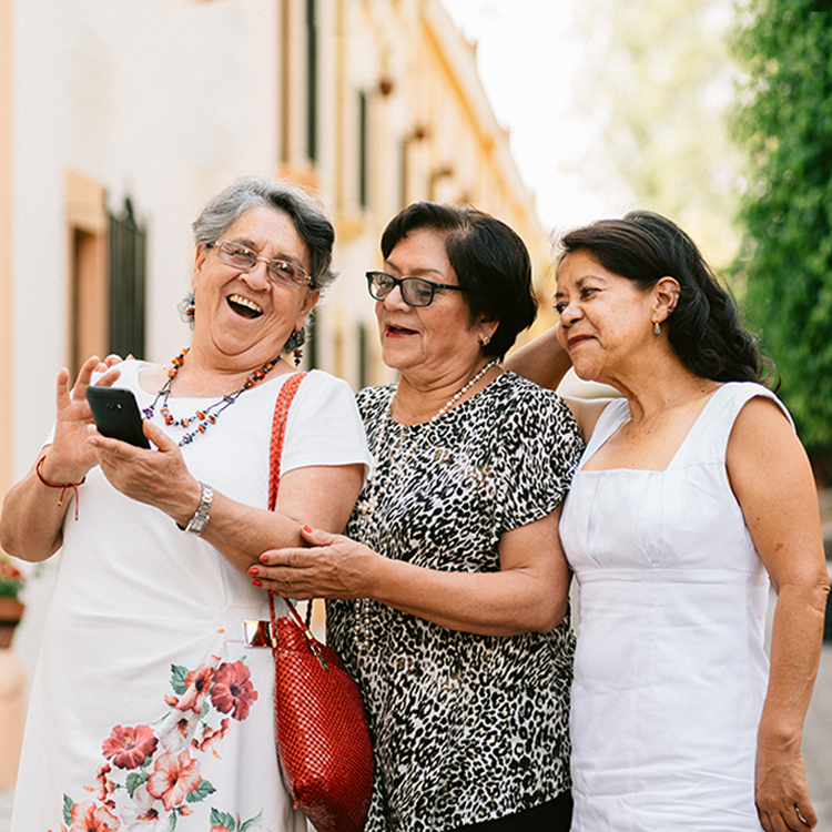 Three senior ladies laughing as they look on a phone