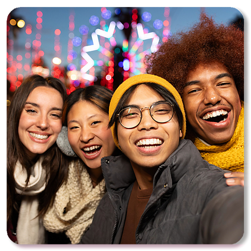 Four students take a selfie in front of a colorful carnival background.