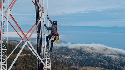 T-Mobile worker climbing tall microwave tower with mountain in background