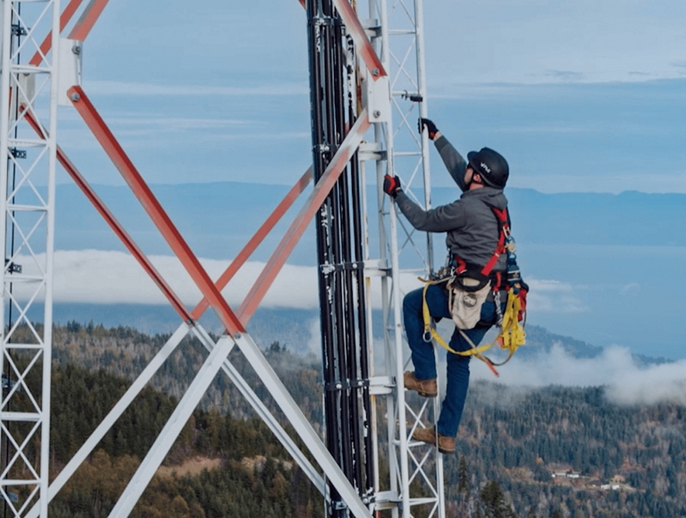 T-Mobile worker climbing tall microwave tower with mountain in background