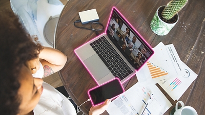 Overhead shot of person holding smartphone while working on a laptop with papers, coffee cup, and cactus surrounding it.