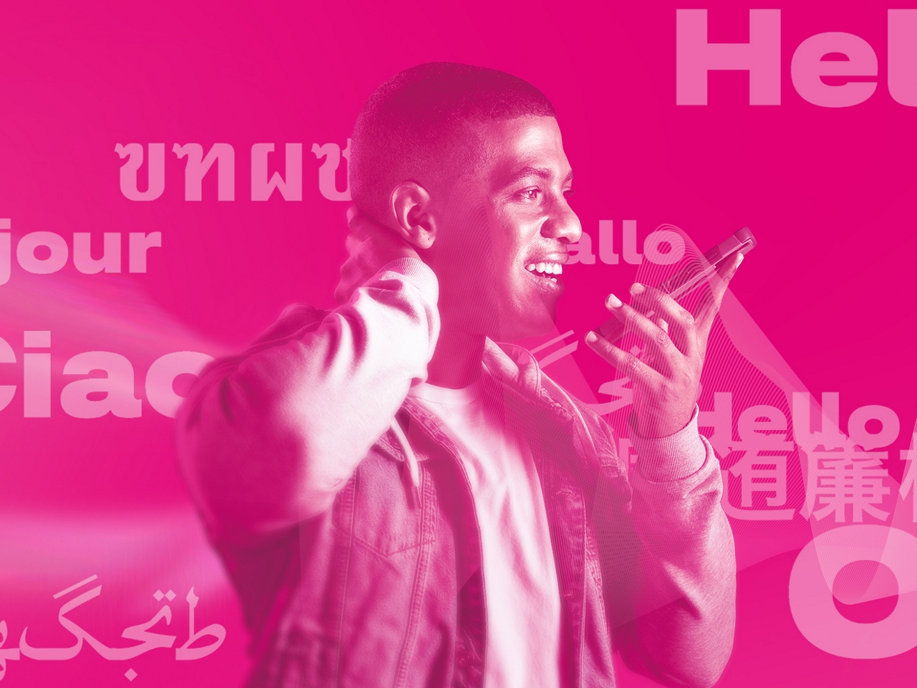 A man in a white t-shirt and denim jacket smiles as he holds a phone up to speak into it. “Hello” in multiple languages appears in magenta behind him.