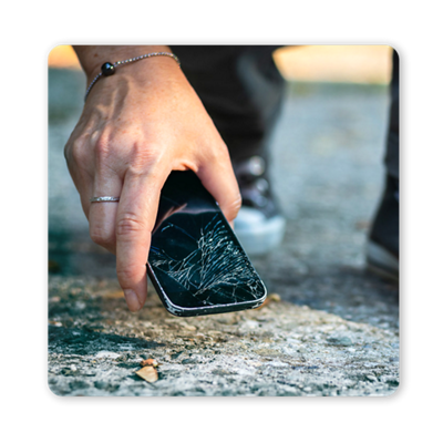 A hand picks up a phone with a shattered screen from the ground.