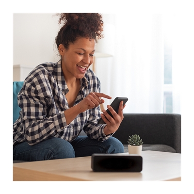 A woman sits on her couch, tapping her phone.