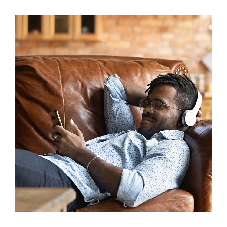 A man on a couch wearing headphones, holding a phone.