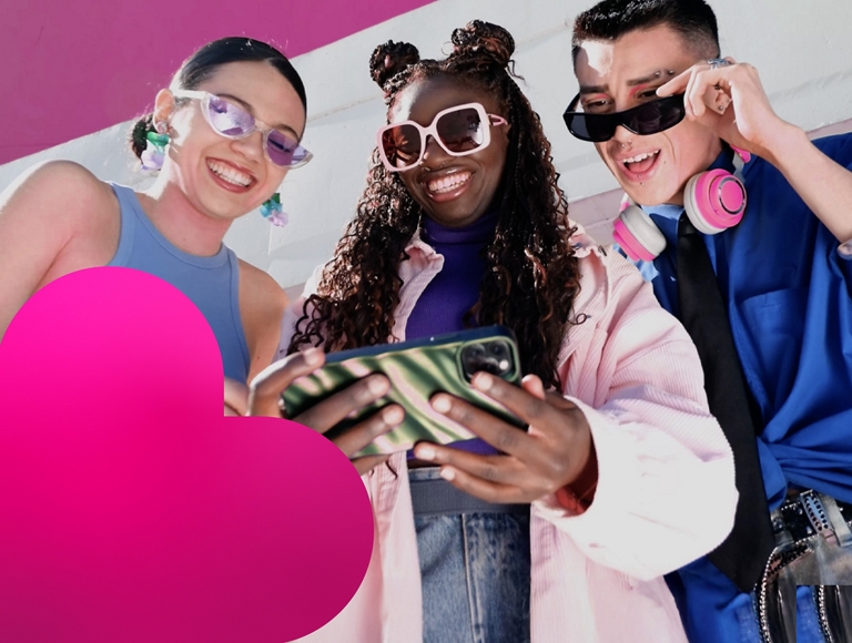 Two women and a man wearing sunglasses smile as they check out something on a phone.