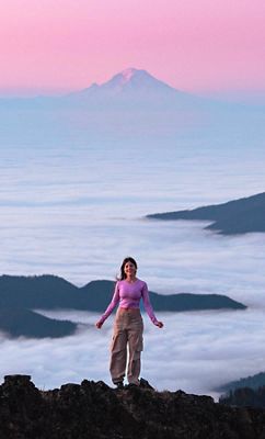 Zoomed out photo of a woman with a pink top and a tall snowy mountain in the background.