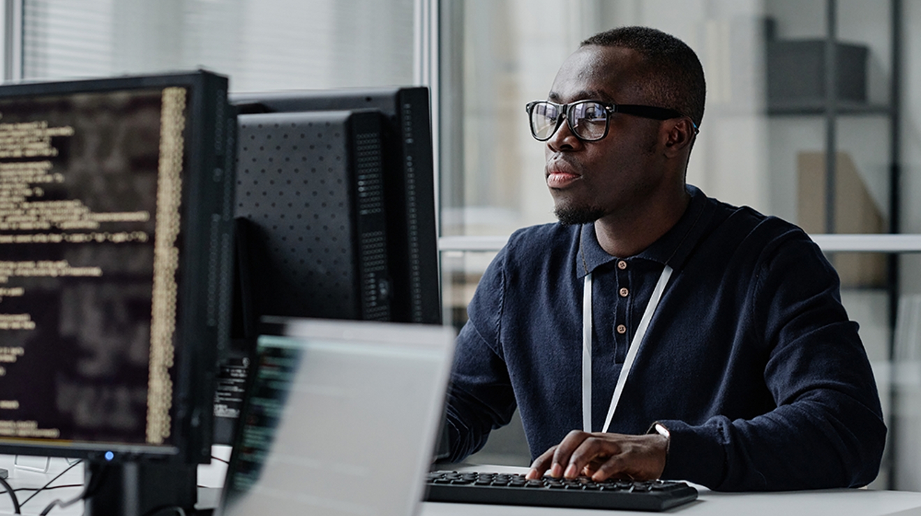 A man sits at a desk in an office, looking at his computer screen. 