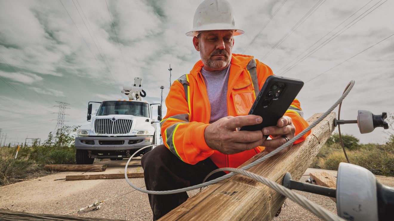 A utility worker in a rural area uses their smartphone to text a teammate.