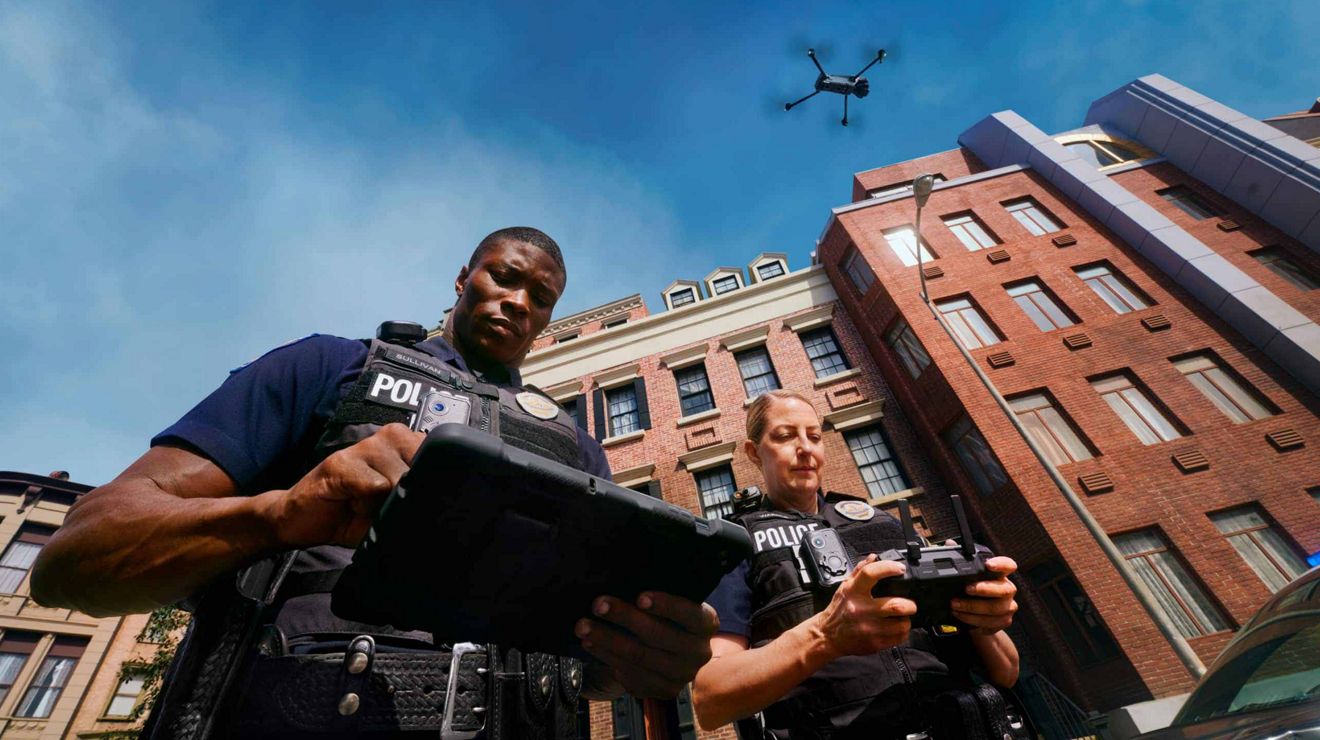 Two police officers operate a drone with a controller and a connected tablet.