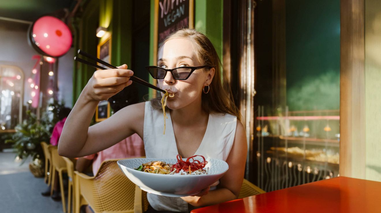 A T-Mobile user enjoys a noodle bowl at an outdoor cafe.