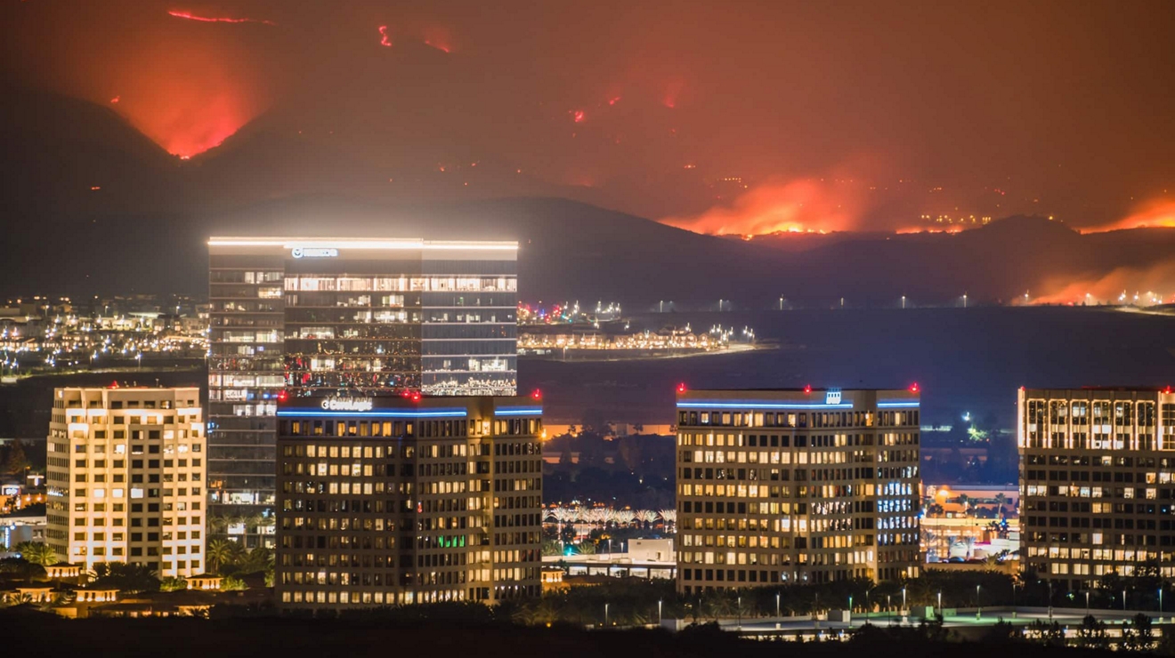 A wildfire burns behind the city skyline at night, highlighting the need for emergency preparedness.