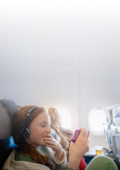 Muchacha joven en un avión con audífonos viendo algo en su teléfono.