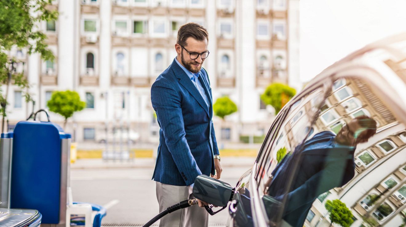 A businessperson dressed for work fills their car with gas.