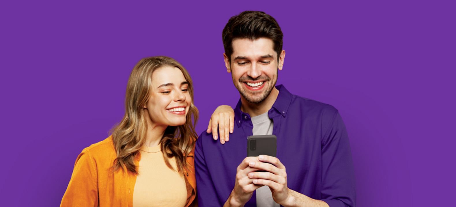 Man and woman smiling while looking at phone.