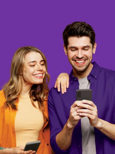 Un hombre y una mujer mirando su teléfono y sonriendo.
