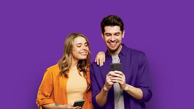 A man and woman smiling while looking at phone.