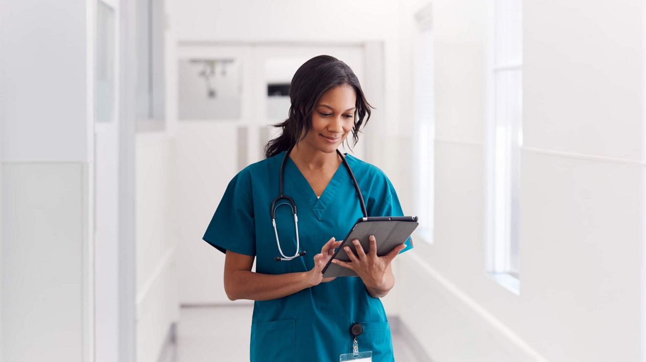 A nurse reviews patient data on a T-Mobile connected tablet while walking across a clinic corridor.