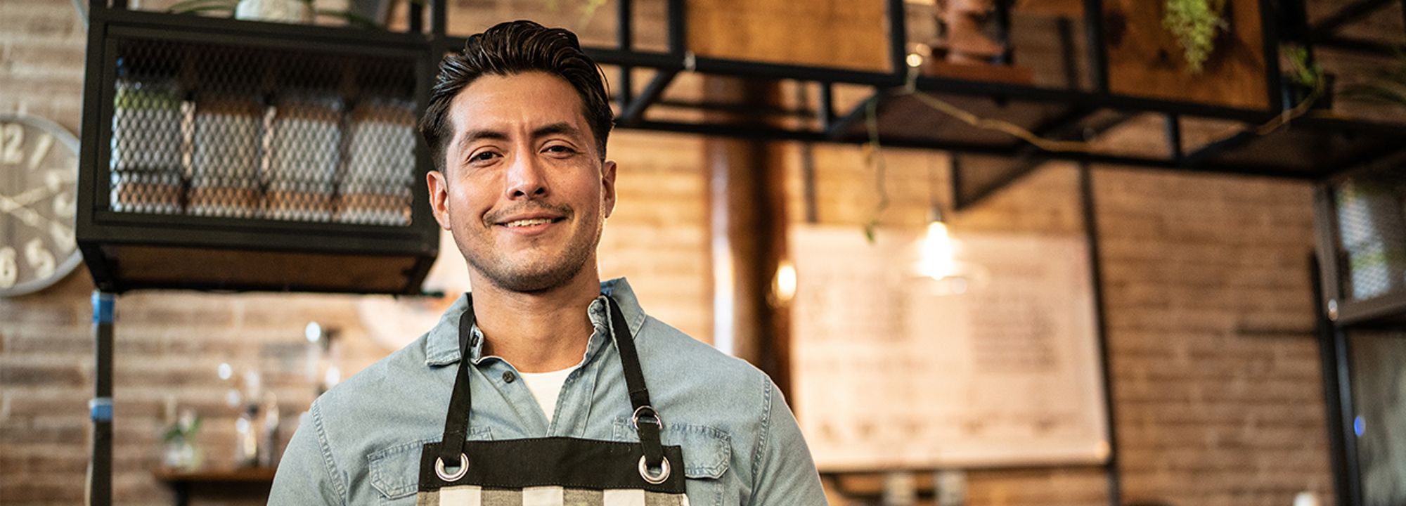 A young adult barista, smiling with a tablet on hand. 