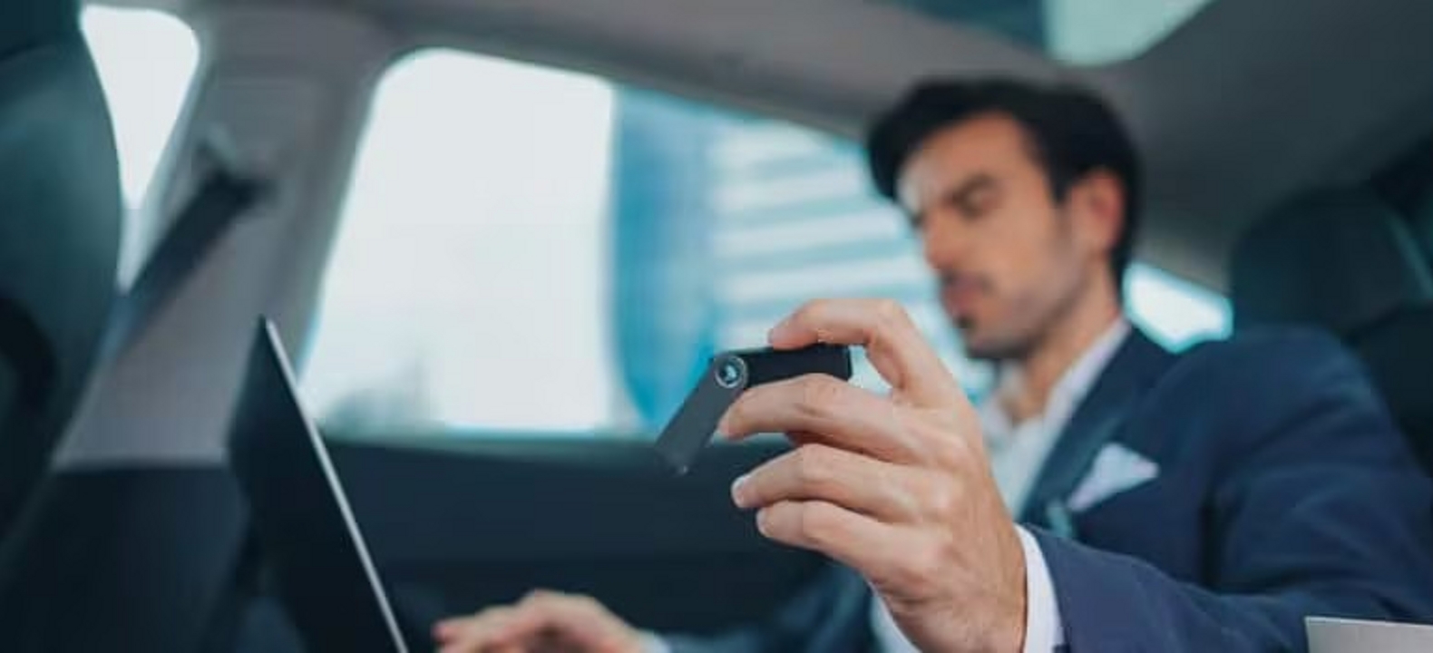 An executive sitting in the back of a car uses a laptop and a passkey.